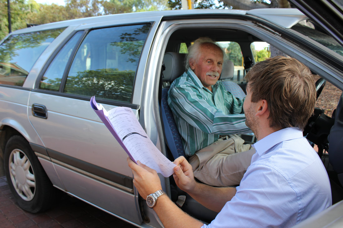 Older gentleman seated in the driver's seat with his Occupational Therapist knelt to his right